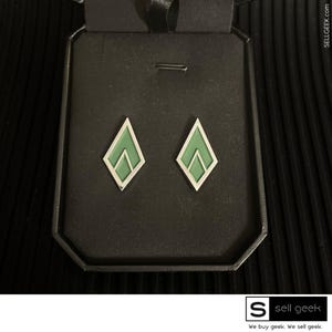 May include: A black velvet box with two green diamond-shaped earrings inside. The earrings are silver and have a geometric design.
