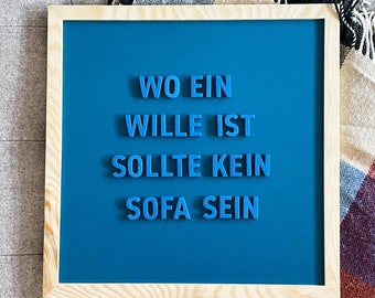 Può includere: Un cartello blu incorniciato in legno con la frase "Wo ein Wille ist sollte kein Sofa sein" in lettere di plastica blu.