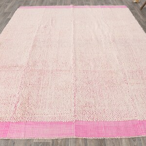 May include: A white and pink shag rug with a pink border. The rug has a textured surface and is made of a soft material.