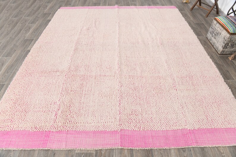 May include: A white and pink shag rug with a pink border. The rug has a textured surface and is made of a soft material.