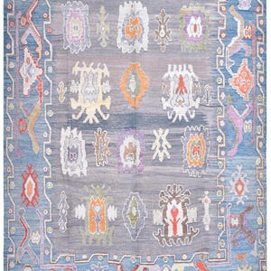 May include: A large, rectangular rug with a blue border and a central field of grey and blue. The rug features a repeating pattern of stylized floral and geometric motifs in shades of orange, purple, and white. The rug measures 4.00 x 3.23 metres.