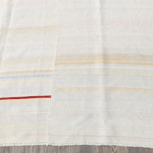 May include: Cream-coloured rug featuring horizontal stripes in beige, light blue, and a bold red accent. The rug has a textured surface and a simple, minimalist design, suitable for various interior styles.