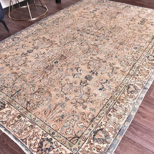 May include: A large, rectangular area rug with an intricate floral pattern in shades of beige, blue, and brown. The rug has a detailed border and a distressed, vintage appearance, suitable for a living room or bedroom.