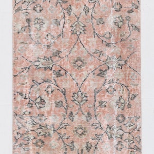May include: A vintage pink and cream rug with a floral pattern. The rug is approximately 3.6 feet by 1.1 feet.