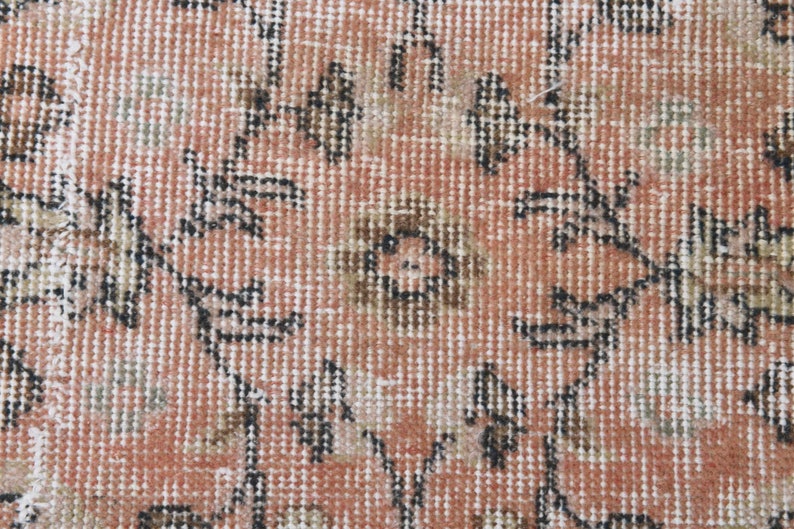May include: Close-up of a pink and white patterned rug with a floral design. The rug has a distressed look and is made of a woven material.