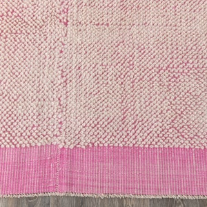 May include: A pink and white bath mat with a fluffy texture. The mat has a pink border with white stripes.