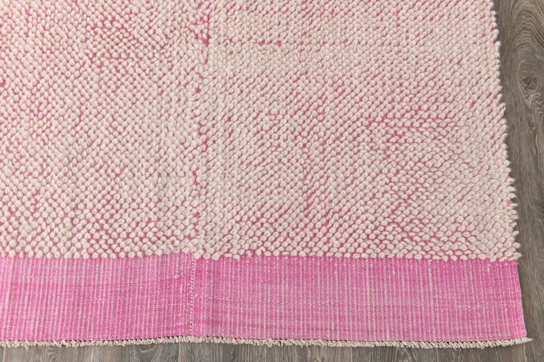 May include: A pink and white bath mat with a fluffy texture. The mat has a pink border with white stripes.