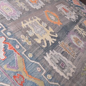 May include: A large, rectangular rug with a faded, distressed look. The rug has a muted colour palette of blues, greys, and accents of orange, purple, and cream. The design includes geometric and floral patterns, creating a vintage aesthetic.