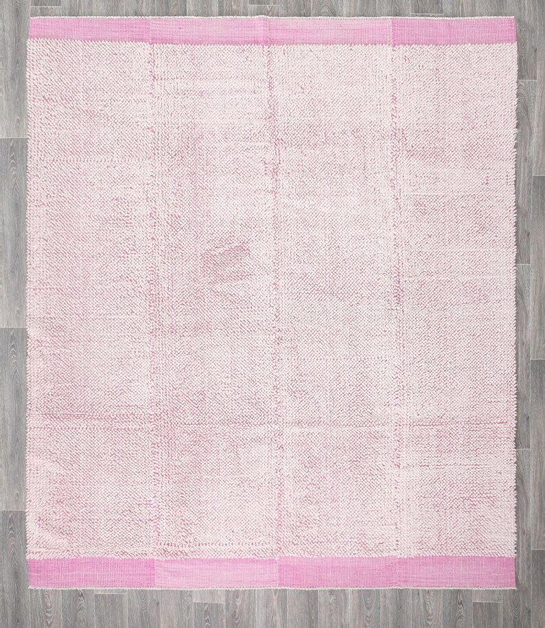 May include: A pink and white fluffy rug with a pink border. The rug has a textured surface and is made of a soft material.