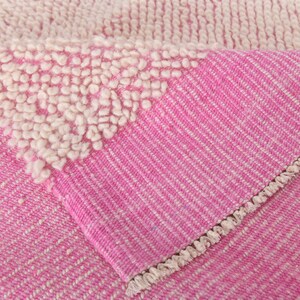 May include: Close-up of a pink and white woven rug with a fringe border. The rug has a textured surface with a pattern of small white loops.