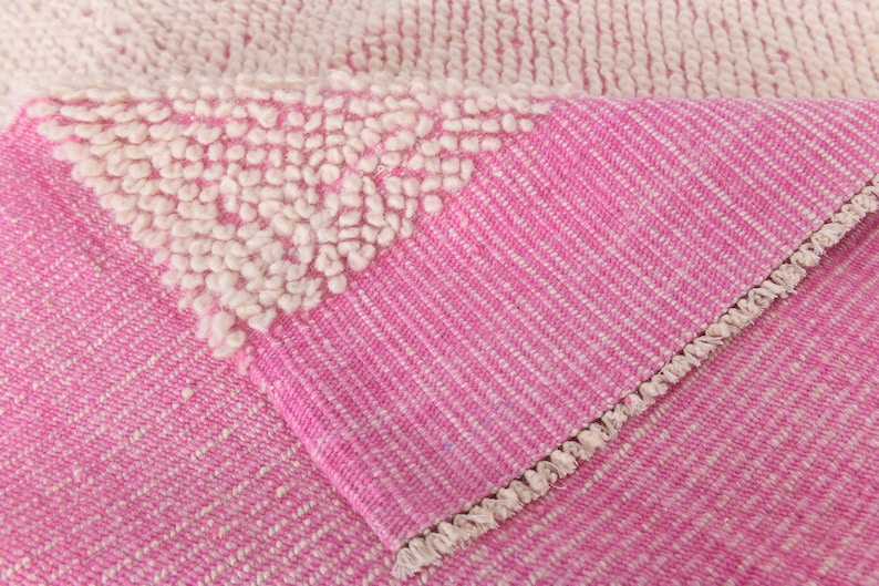 May include: Close-up of a pink and white woven rug with a fringe border. The rug has a textured surface with a pattern of small white loops.