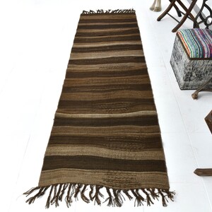 May include: A long, brown and beige striped rug with fringe on the ends. The rug is woven with a textured pattern.