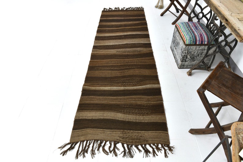 May include: A long, brown and beige striped rug with fringe on the ends. The rug is woven with a textured pattern.