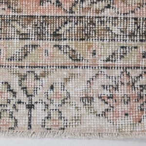 May include: Close-up of a cream-colored rug with a floral pattern in shades of brown, pink, and black. The rug has a fringe border.