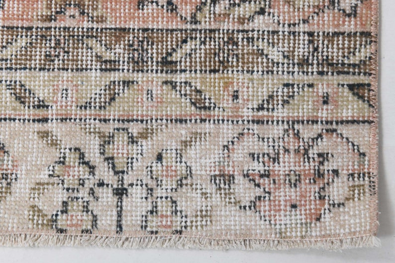 May include: Close-up of a cream-colored rug with a floral pattern in shades of brown, pink, and black. The rug has a fringe border.