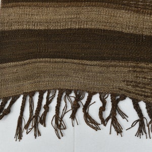 May include: A brown woven rug with a fringe border. The rug has a striped pattern with different shades of brown.
