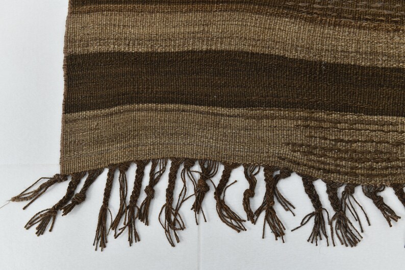 May include: A brown woven rug with a fringe border. The rug has a striped pattern with different shades of brown.