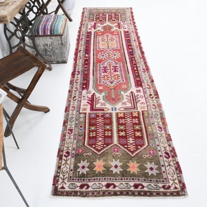 K&ouml;nnte beinhalten: Ein antiker t&uuml;rkischer L&auml;ufer mit einem geometrischen Muster in Rot, Rosa und Gr&uuml;n. Der Teppich hat einen wei&szlig;en Hintergrund und einen Fransenrand.
