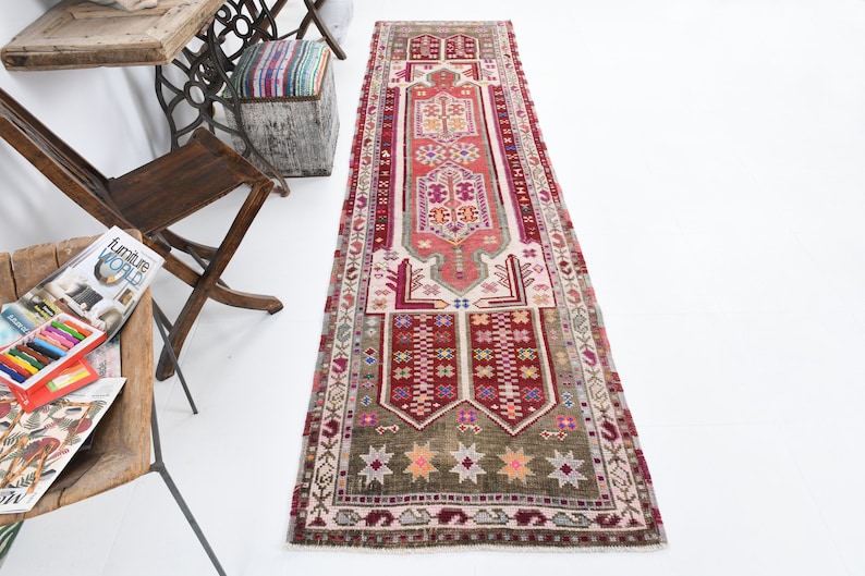 K&ouml;nnte beinhalten: Ein antiker t&uuml;rkischer L&auml;ufer mit einem geometrischen Muster in Rot, Rosa und Gr&uuml;n. Der Teppich hat einen wei&szlig;en Hintergrund und einen Fransenrand.