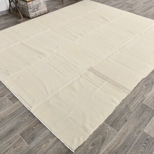 May include: A large, off-white, rectangular rug with a subtle woven texture. The rug is made of natural fibers and has a simple, minimalist design.