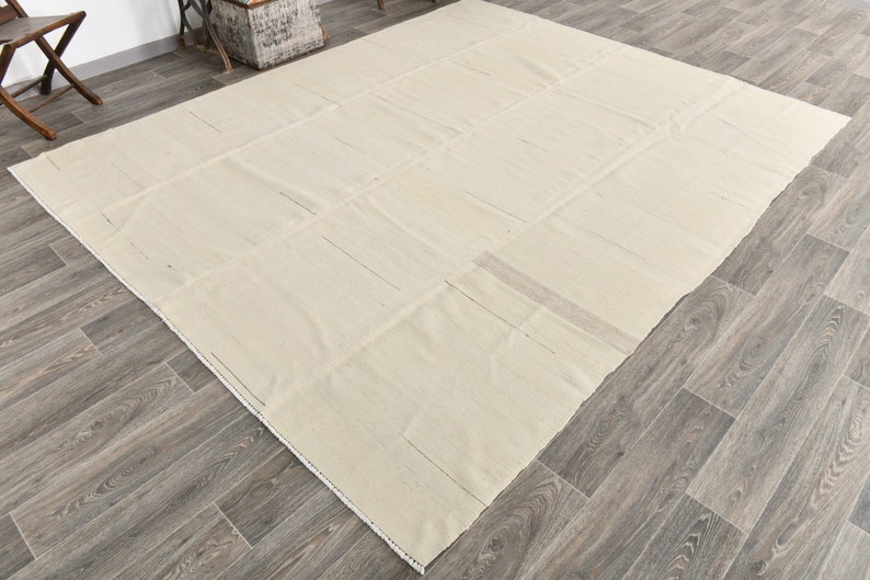 May include: A large, off-white, rectangular rug with a subtle woven texture. The rug is made of natural fibers and has a simple, minimalist design.