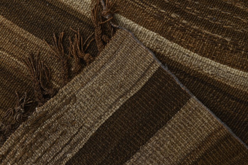 May include: Close-up of a brown and beige striped woven rug with fringe on the edges.