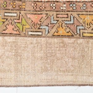 May include: Close-up of the back of a rug with a brown fringe. The rug has a beige background with a colorful geometric pattern.