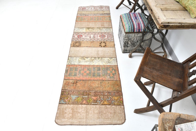 May include: A long, rectangular rug with a patchwork design. The rug is made of different colored fabrics with geometric patterns. The rug is beige, brown, and orange with a hint of pink.