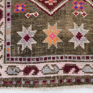 K&ouml;nnte beinhalten: Ein brauner Teppich mit einem geometrischen Muster in Rosa-, Rot-, Orange- und Wei&szlig;t&ouml;nen. Der Teppich hat einen Fransenrand.