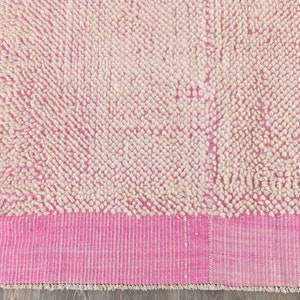 May include: A pink and white shag rug with a pink border. The rug has a fluffy texture and is made of wool.