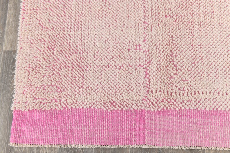 May include: A pink and white shag rug with a pink border. The rug has a fluffy texture and is made of wool.