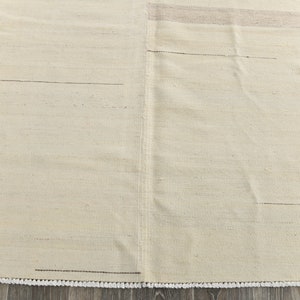 May include: A cream-colored rug with a subtle woven texture and a fringe border.