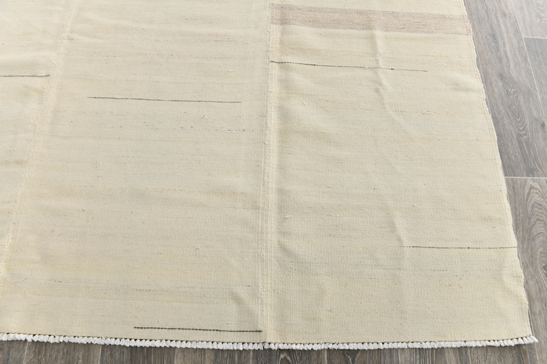 May include: A cream-colored rug with a subtle woven texture and a fringe border.