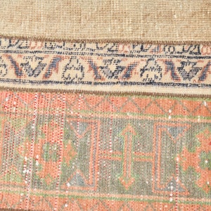 May include: Close-up of a vintage rug with a faded floral pattern in shades of pink, green, and blue. The rug has a brown fringe border.