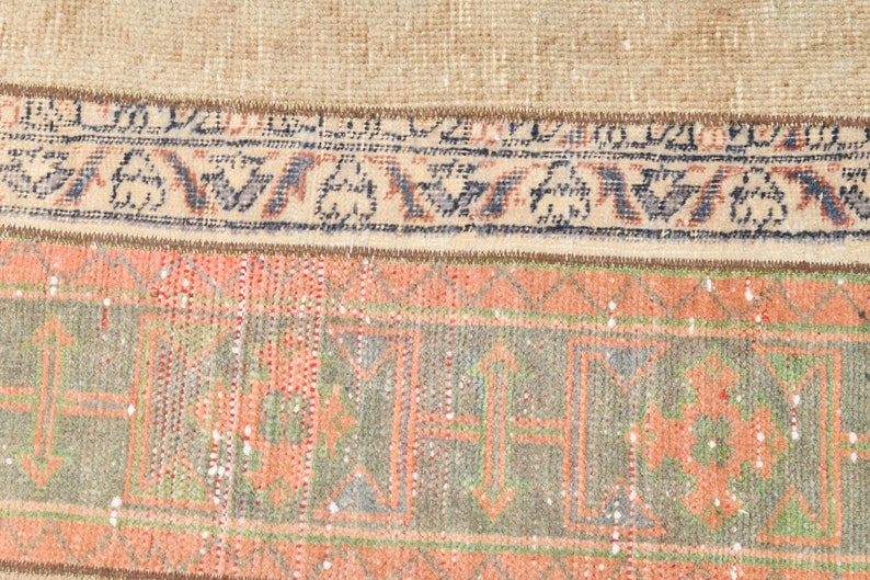May include: Close-up of a vintage rug with a faded floral pattern in shades of pink, green, and blue. The rug has a brown fringe border.