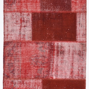 以下が含まれることがあります： さまざまな質感とパターンを持つ赤いパッチワークラグ。ラグは、縫い合わせられたさまざまな生地のピースで構成されています。