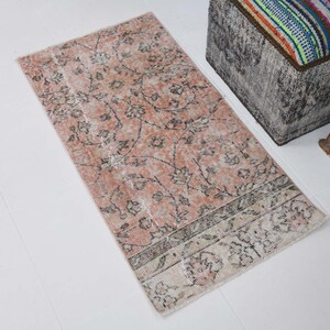 May include: A pink and cream patterned rug with a floral design. The rug has a faded look and is made of a soft, woven material.