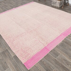 May include: A cream-colored rug with a pink border. The rug has a textured surface and is made of a soft material.