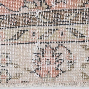 May include: Close-up of a pink and cream patterned rug with a fringe border. The rug has a floral design with intricate details.
