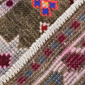 K&ouml;nnte beinhalten: Nahaufnahme eines gewebten Teppichs mit Fransenbord&uuml;re. Der Teppich zeigt ein geometrisches Muster in Braun-, Rosa- und Blaut&ouml;nen.