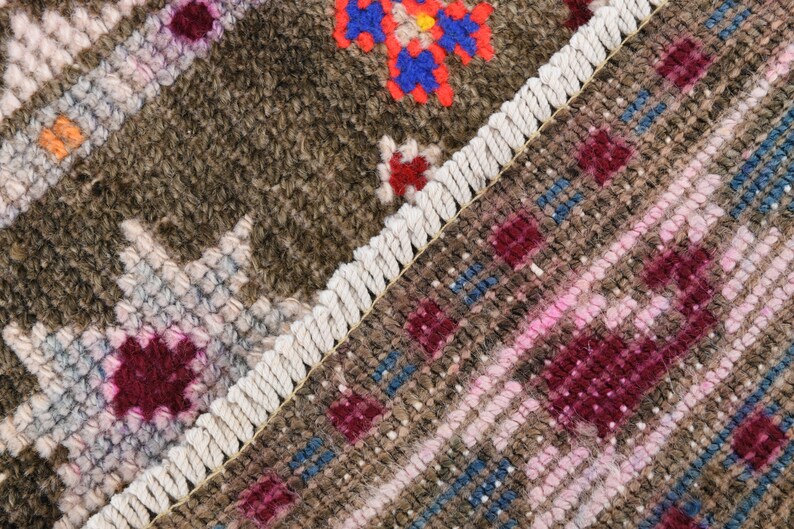 K&ouml;nnte beinhalten: Nahaufnahme eines gewebten Teppichs mit Fransenbord&uuml;re. Der Teppich zeigt ein geometrisches Muster in Braun-, Rosa- und Blaut&ouml;nen.