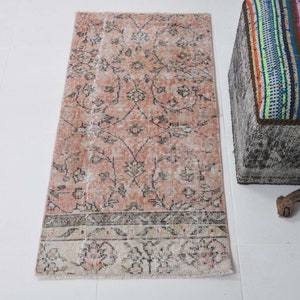 May include: A pink and white vintage floral patterned rug with a faded look. The rug has a fringe border and is approximately 2 feet wide and 6 feet long.
