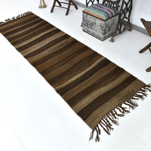 May include: A brown and beige striped runner rug with fringe on the ends. The rug is laying on a white floor.