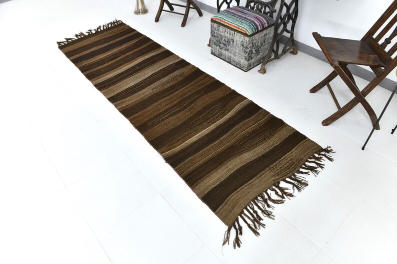 May include: A brown and beige striped runner rug with fringe on the ends. The rug is laying on a white floor.
