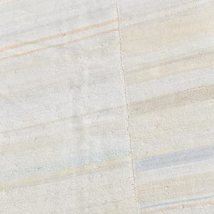 May include: Close-up of a textured, off-white rug with subtle horizontal stripes in beige and light blue. The rug has a soft, neutral colour palette, suitable for various interior styles. The rug's design is simple and elegant.