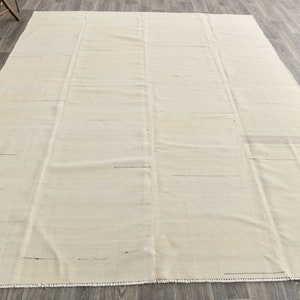 May include: A plain white rug with a subtle woven texture. The rug has a fringe border and is laid out on a wooden floor.