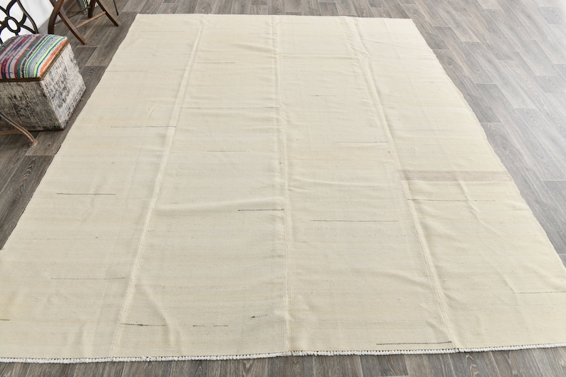 May include: A plain white rug with a subtle woven texture. The rug has a fringe border and is laid out on a wooden floor.