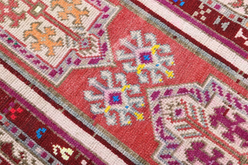 K&ouml;nnte beinhalten: Nahaufnahme eines bunten gewebten Teppichs mit einem geometrischen Muster in den Farben Rosa, Rot, Wei&szlig; und Blau.