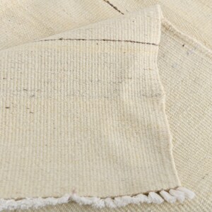 May include: A close-up of a white woven rug with a fringe border. The rug is made of natural fibers and has a subtle texture.