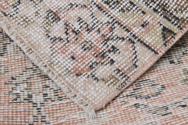May include: Close-up of a woven rug with a pink, white, and brown geometric pattern. The rug has a fringed edge.